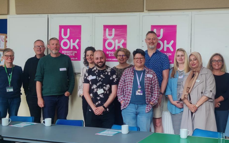 UOK Partners representatives stand in a group against a backdrop of UOK poster.