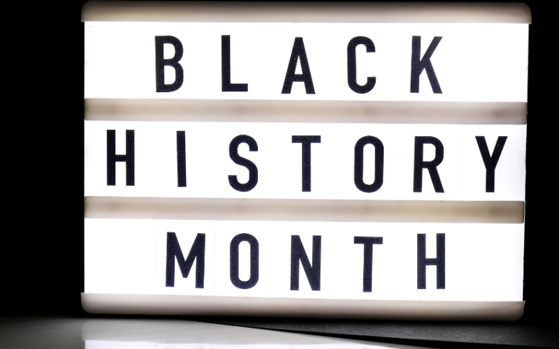 On a black background, words 'BLACK HISTORY MONTH' are written backlit on a white block.