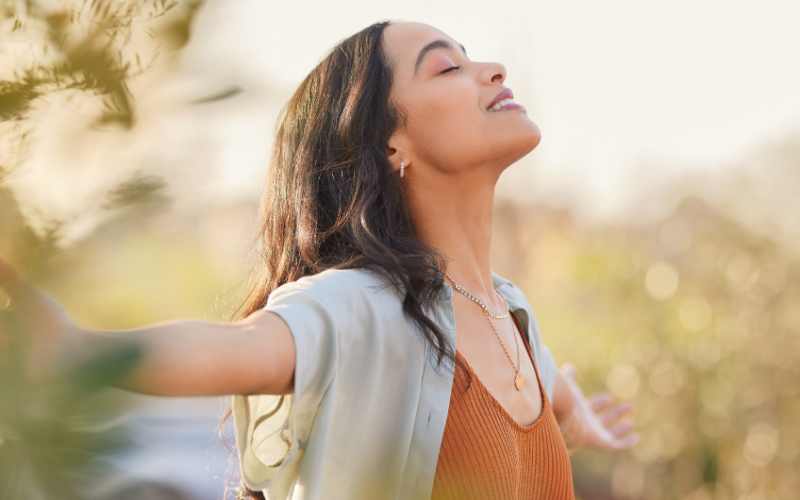 A girl wearing an ochre tshirt and overshirt with her arms wide open, eye closed representing peaceful mind.