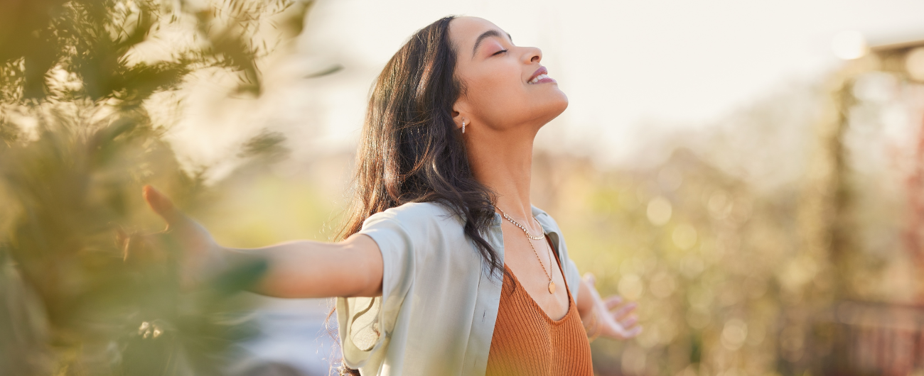 A girl wearing an ochre tshirt and overshirt with her arms wide open, eye closed representing peaceful mind.